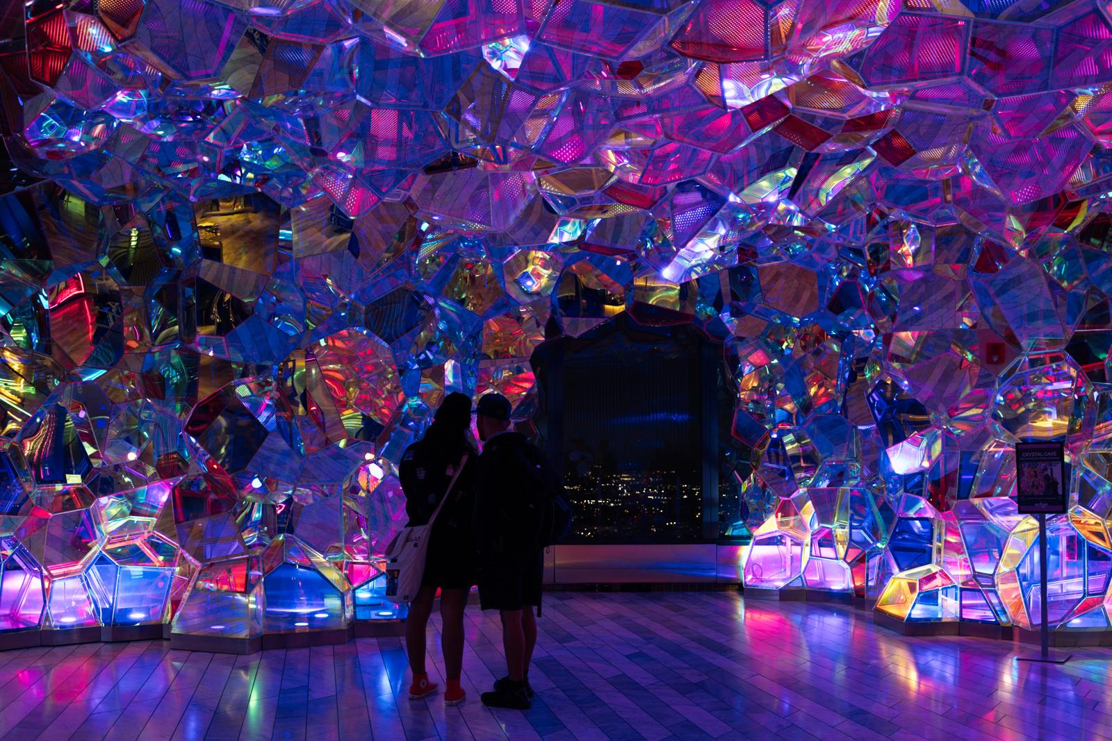 Pick: two people inside a room of mirrored prisms lit pink and blue